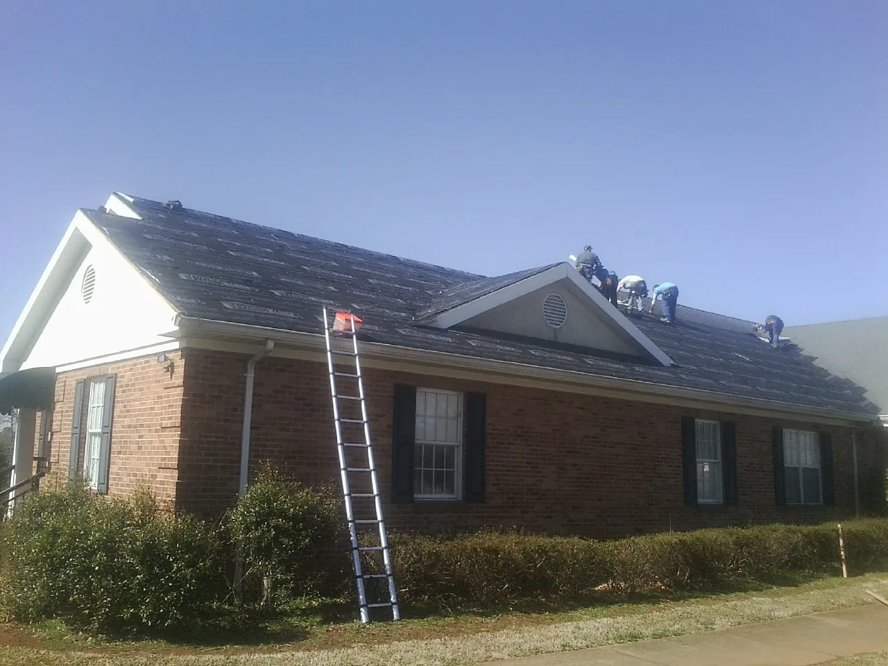Crew tearing shingles off a brick ranch roof with a ladder set — Emergency Roof Repair work by our crew in Morning View