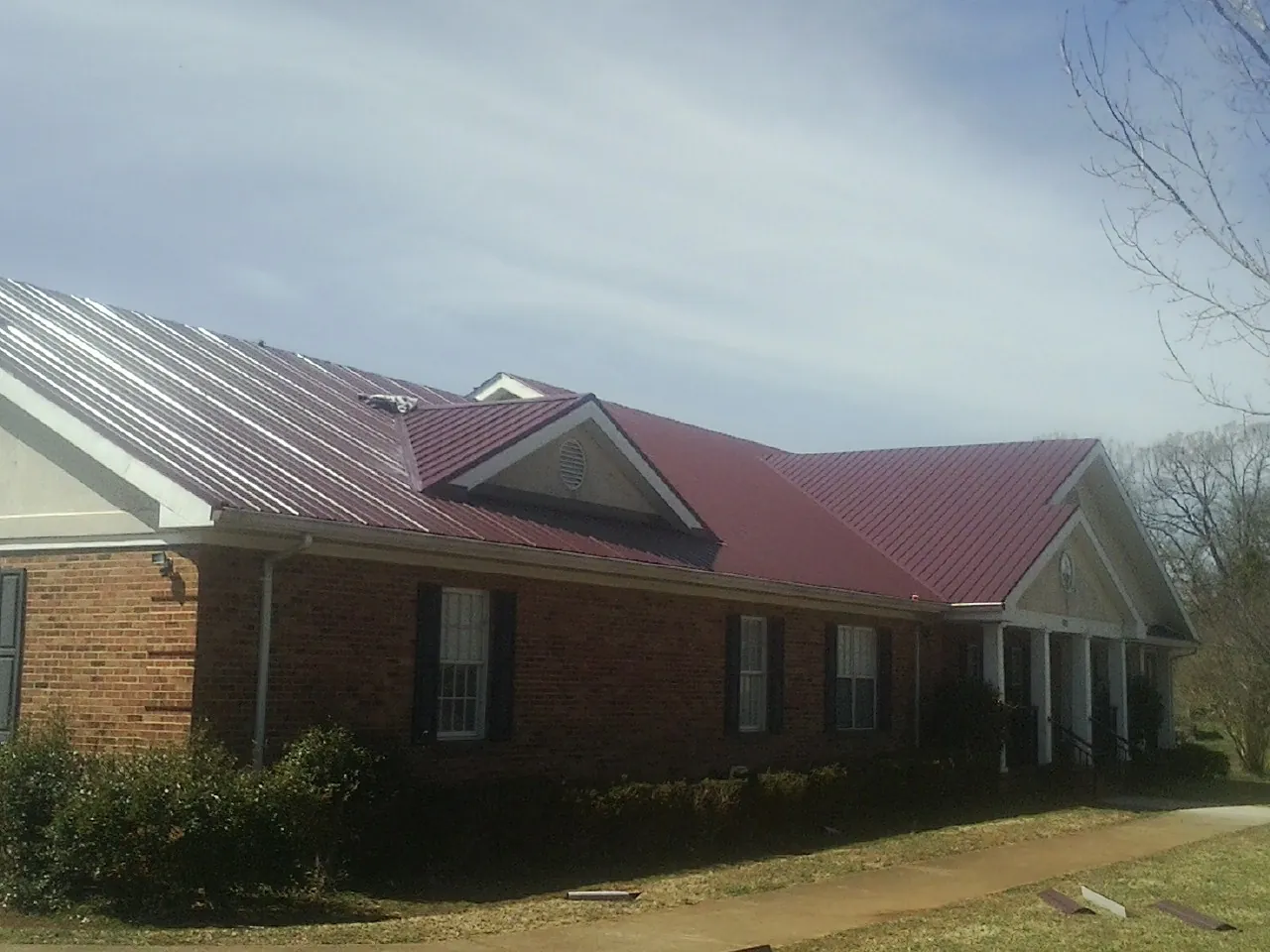 Red metal roof with gabled entries on a long brick building, from a Hail Damage Roof Repair job in Morning View