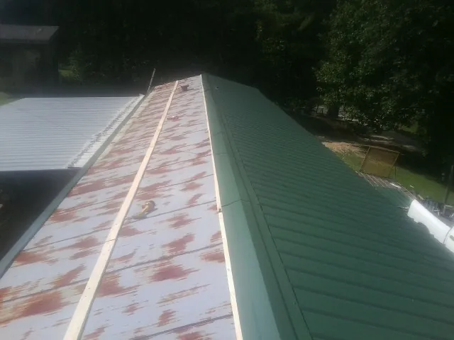 Old rusted panels beside newly installed green metal roofing — Wind Damage Roof Repair by Roofing Brothers in Morning View