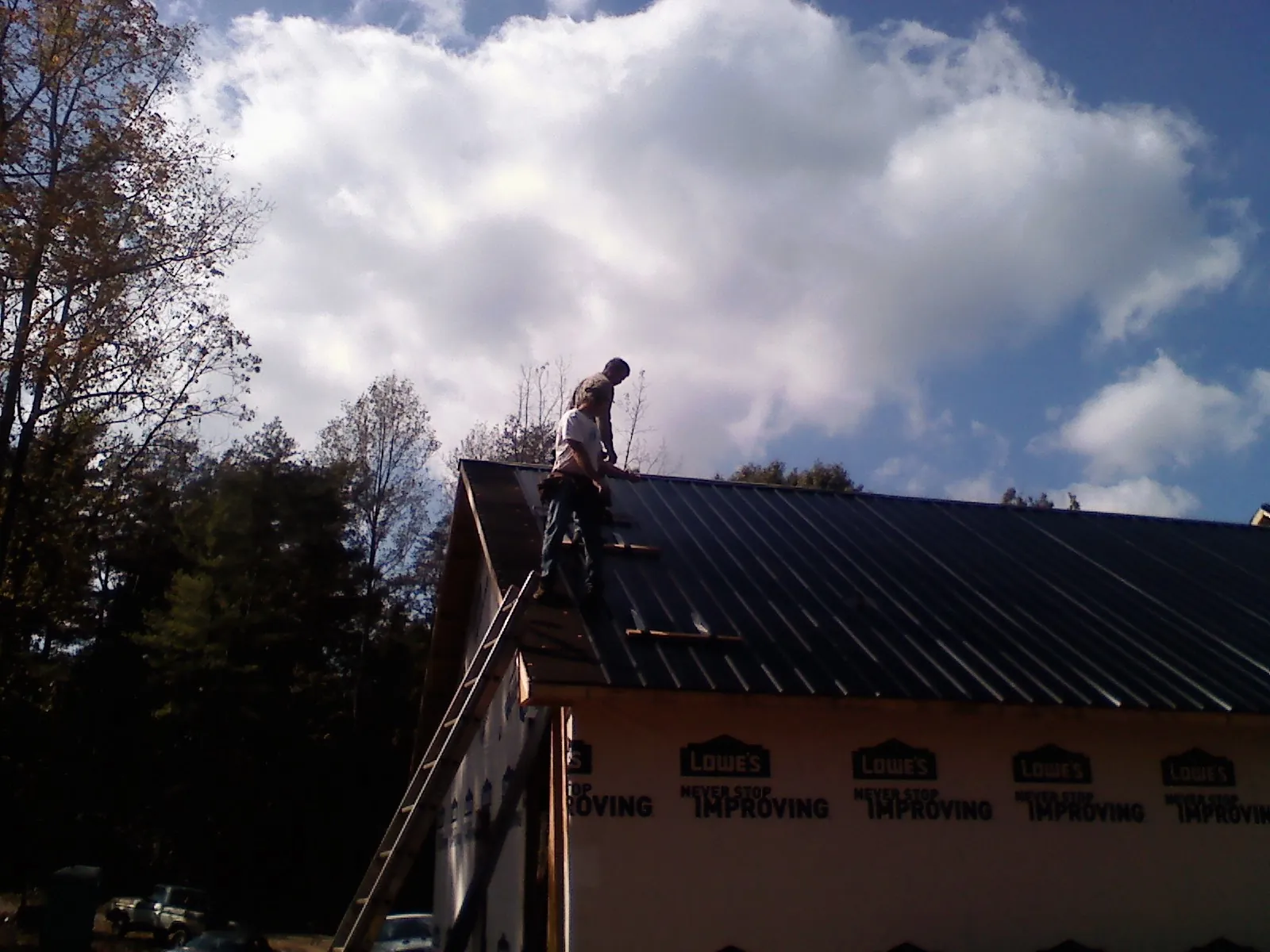 Roofer fastening dark metal panels high against a cloudy sky, from a Roof Inspection job in Morning View