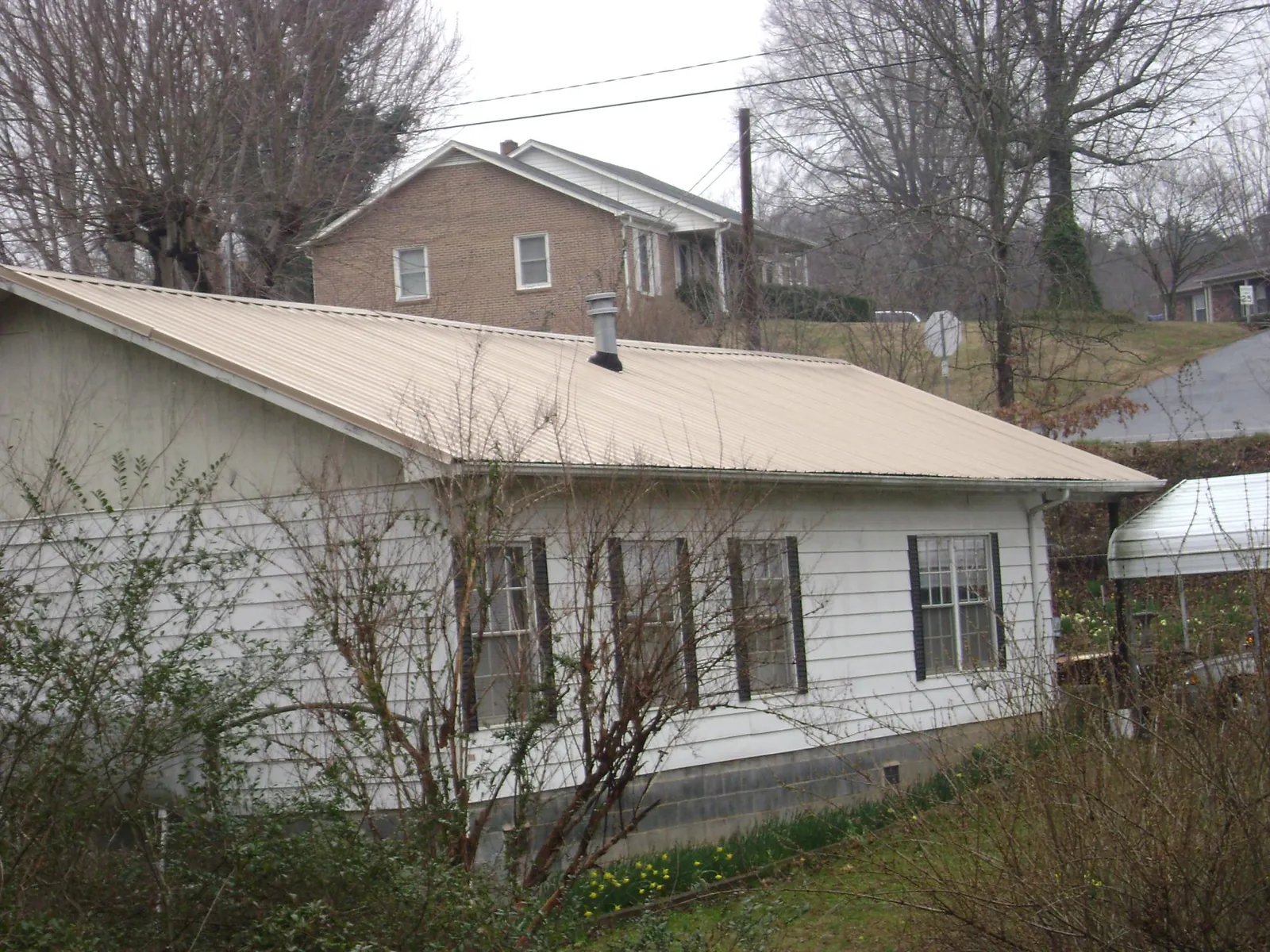Tan metal roof on a white sided house set into a hillside — Commercial Roofing by Roofing Brothers in Morning View